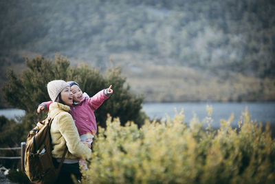 Mother carrying daughter while standing by plants