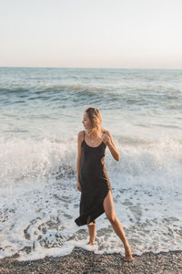 A girl in a black flowing dress stands in the water on the beach