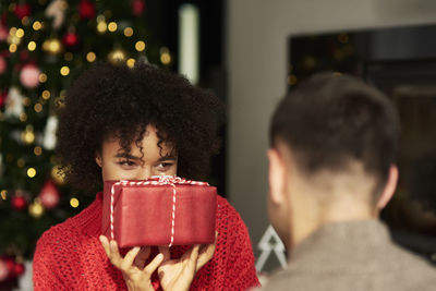 Smiling woman holding christmas present in front of man at home