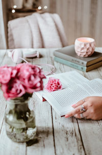 Cropped hand of woman holding book by vase at table