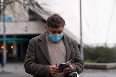 Outdoor portrait of a man covering his face with a medical mask looking down at his smartphone