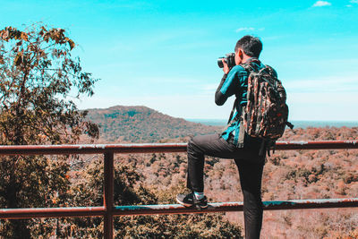 Backpacker photographing landscape while standing by railing