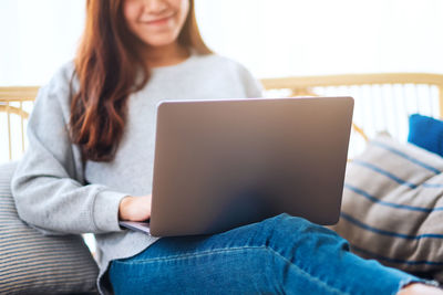 Midsection of woman using laptop while sitting on sofa at home