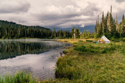 Lake side camp site with tent, illuminated under ominous sky.