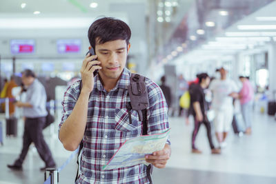 Young man talking on phone while holding map at airport