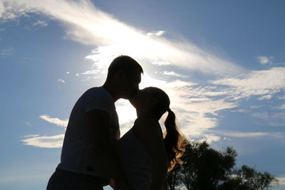 Side view of young couple kissing against sky