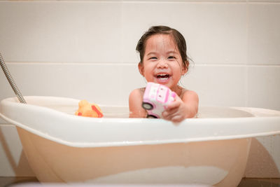 Portrait of smiling girl playing with toy in bathtub