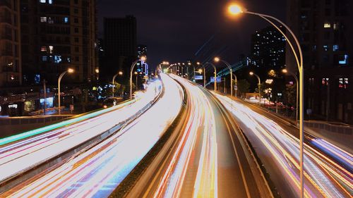 Light trails on road by illuminated buildings at night