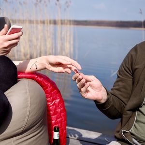 Close-up of hands holding mobile phone against sea