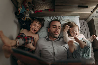 High angle view of father reading book for children while lying on bed at home