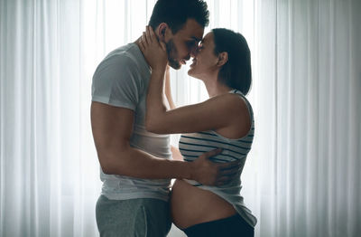 Side view of young couple standing against window