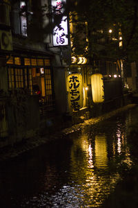 Illuminated buildings by canal in city at night