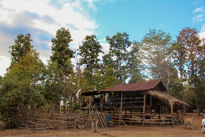 Abandoned house by trees on field against sky