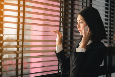 Woman looking away while standing against window