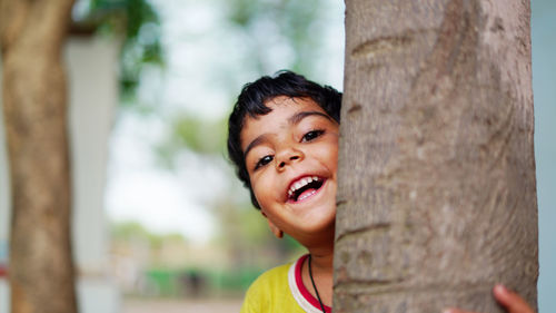 Portrait of boy smiling against tree trunk
