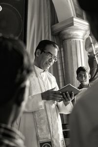 Priest reading book by people in church