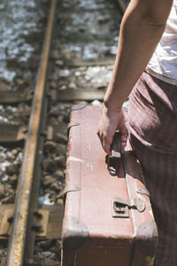 Midsection of woman holding suitcase while standing on railroad track