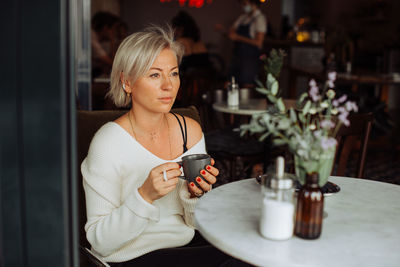 Blond woman holding cup of tea while sitting alone at table in cafe