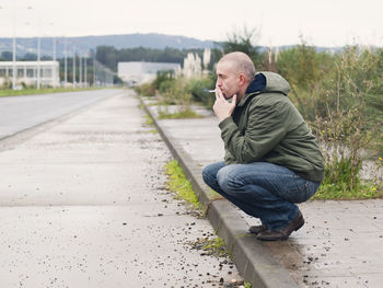 Man smoking while crouching on footpath during winter