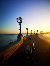 Street light by sea against clear sky during sunset