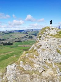 Distant view of young woman standing on cliff against sky