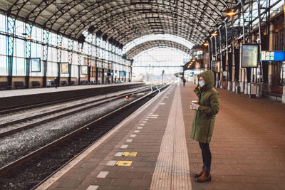 Woman wearing a mask standing on railroad station platform