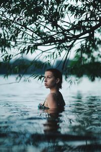 Young woman sitting in lake against sky