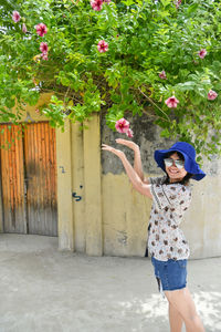 Portrait of smiling young woman wearing hat while standing against wall