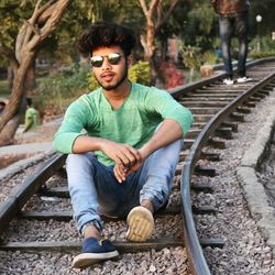 Portrait of young man wearing sunglasses sitting on railroad track