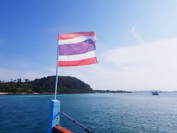 Flag on pole by sea against sky