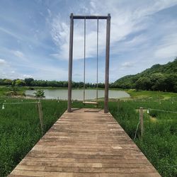 Wooden walkway amidst plants on field against sky