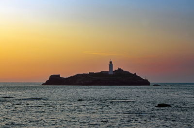 Lighthouse by sea against sky during sunset