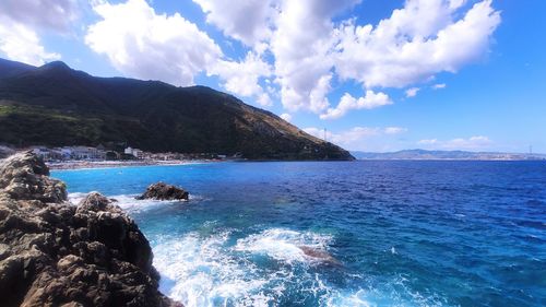 Scenic view of sea by mountain against sky