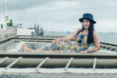 Woman sitting on netting over sea against sky