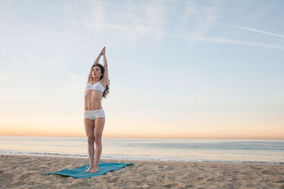 Full length of woman meditating at beach against sky