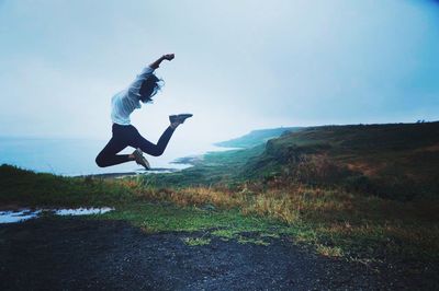 Woman jumping on grassy mountain against sky