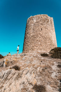 Low angle view of man on rock against clear blue sky