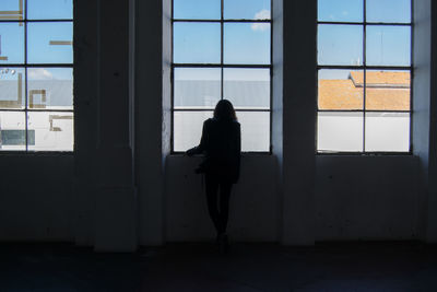 Silhouette woman looking through window