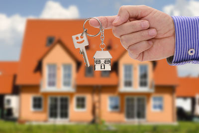 Cropped hand of real estate agent holding key against house