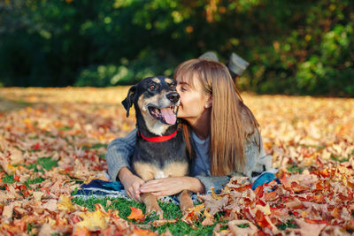 Young woman with dog lying on leaves during autumn