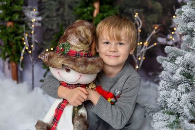 Portrait of smiling boy holding christmas tree during winter