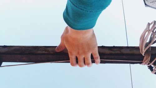Cropped image of hand holding wooden railing against clear sky