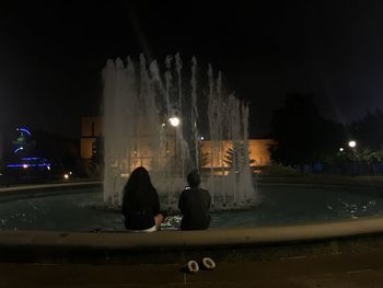 Rear view of people sitting in illuminated city at night