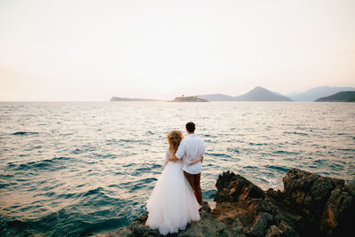 Rear view of couple standing near sea against sky