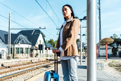 Young woman standing on railroad track against sky