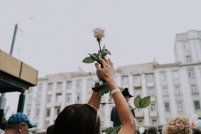 People holding flowering plant in city against sky