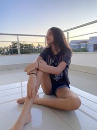 Girl sitting by railing against clear sky