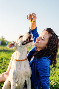 Woman feeding dog on grassy land against clear sky