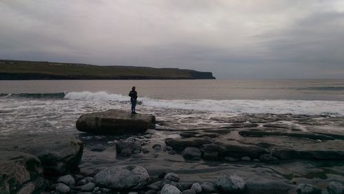 Man standing on rock by sea against sky