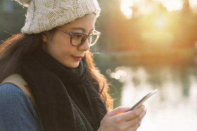 Close-up of young woman using mobile phone against lake